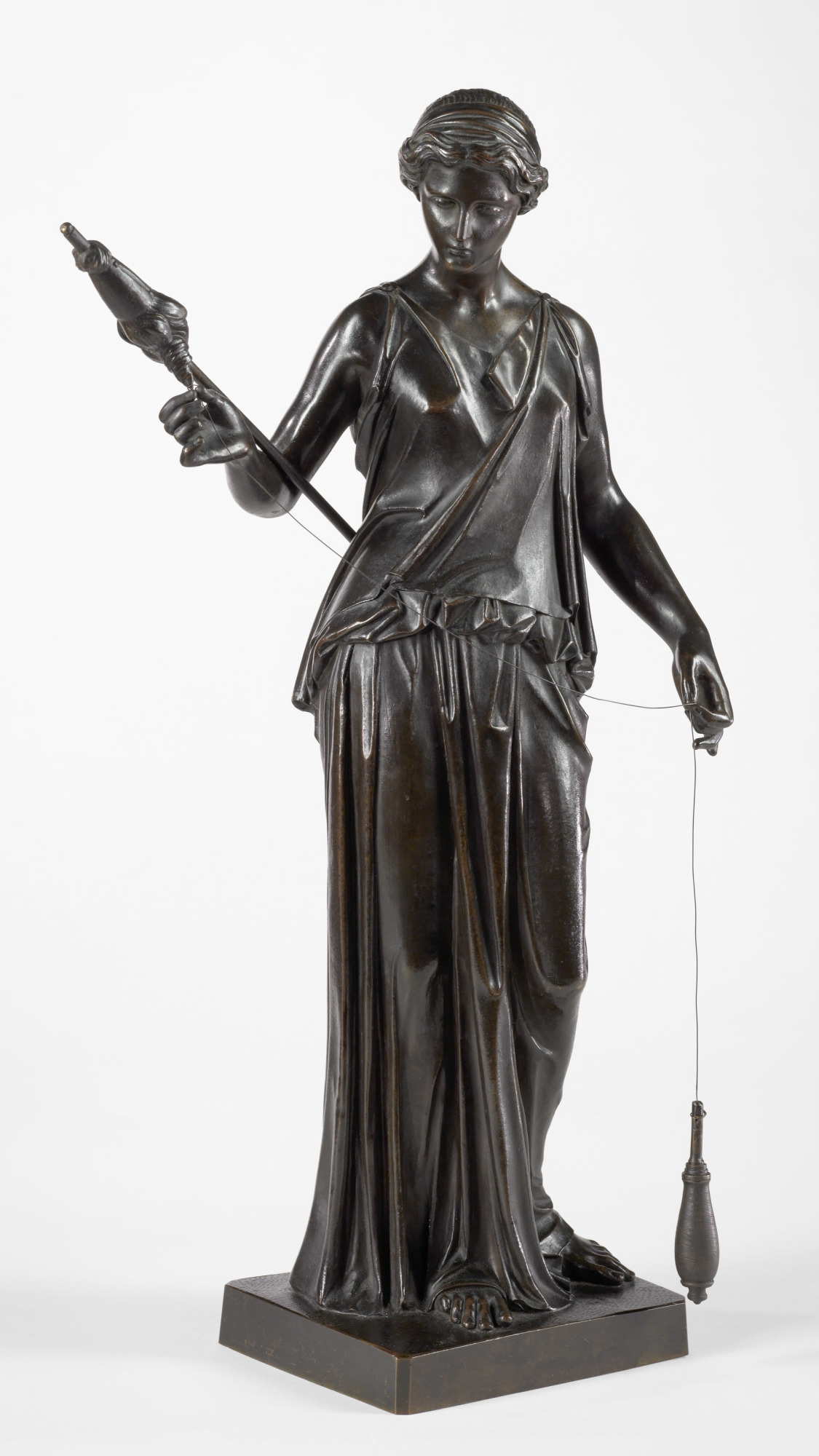 A bronze sculpture of a woman holding a staff in one hand and spooling thread onto a spindle with the other.