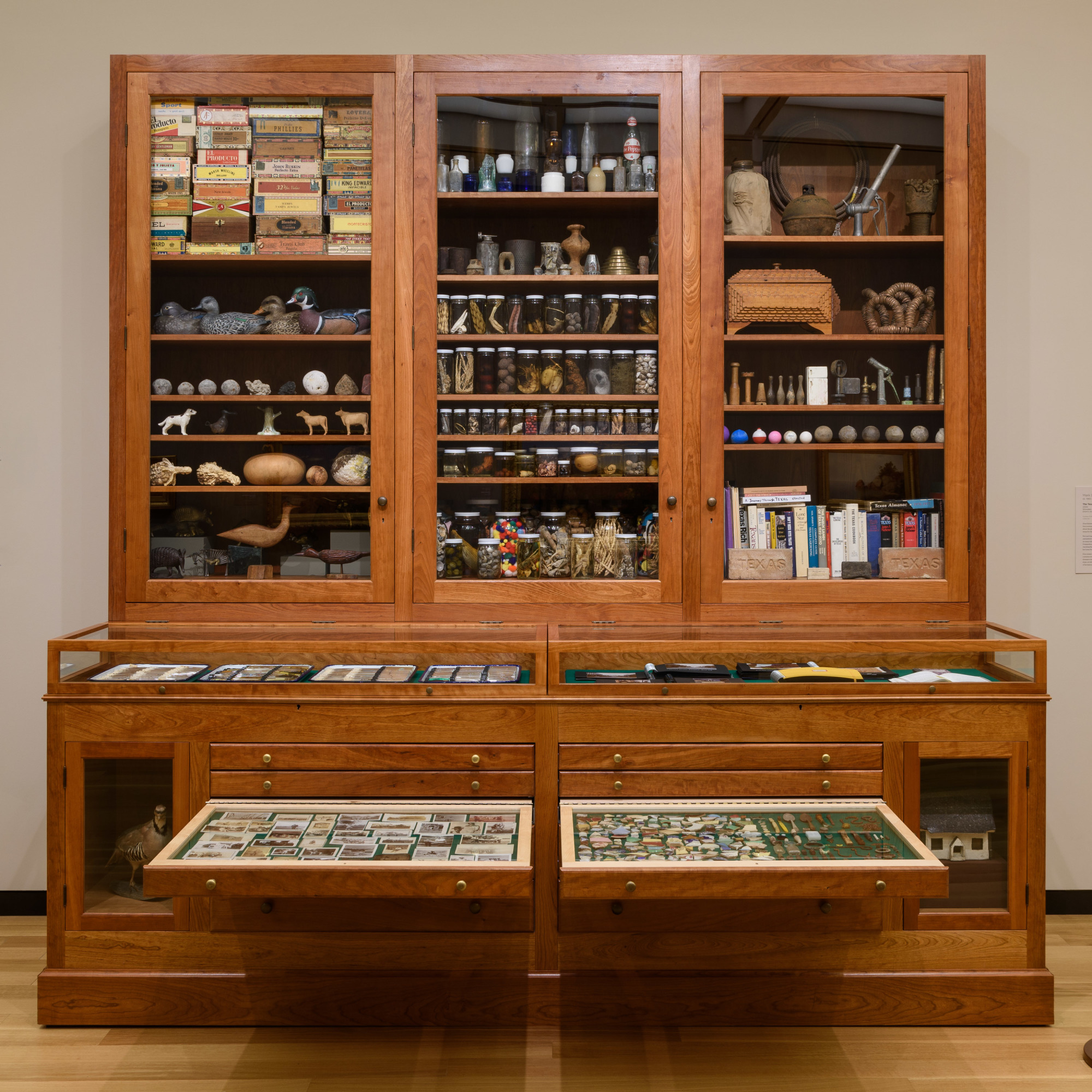 A large wooden cabinet with drawers on the bottom half and glass-fronted cabinets above, all filled with random objects.