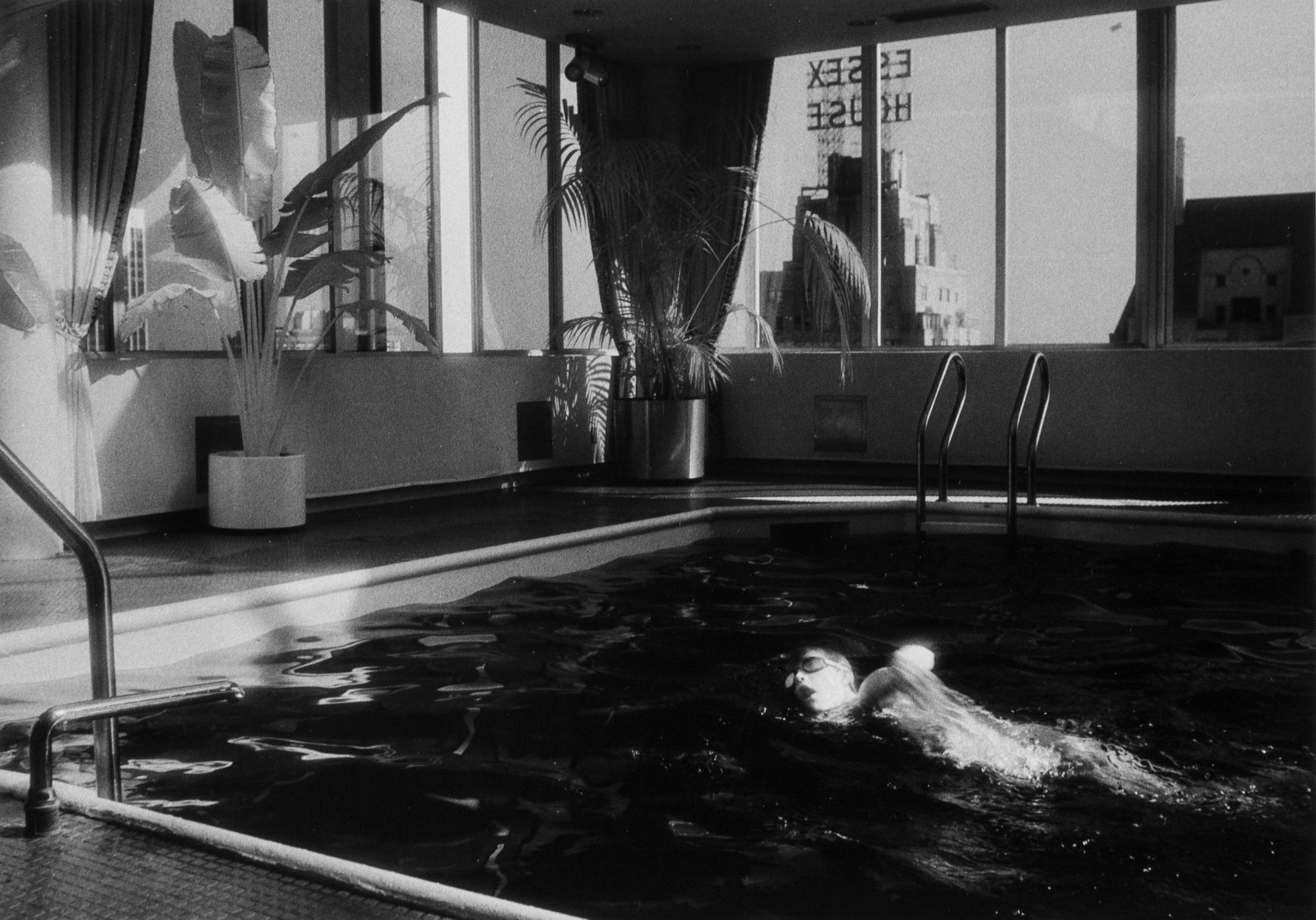 A black-and-white photograph of a person swimming in an indoor pool.