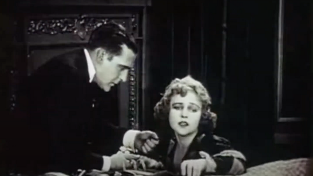 A screen grab showing a White man, holding jewelry in his hands, leaning toward a seated White woman.