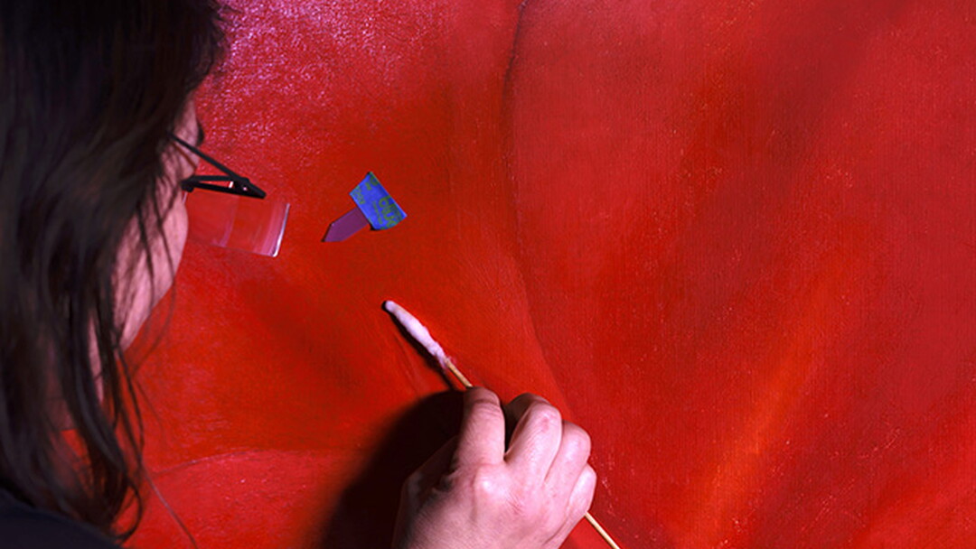 A White woman uses a cotton swab to clean a painting of a red flower.
