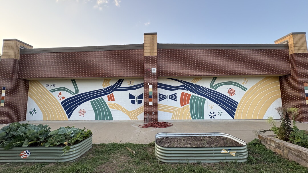 A mural on the side of a building next to several raised garden beds.