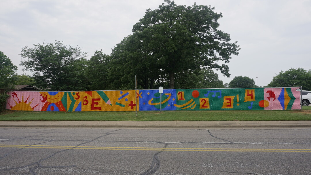 A chain link fence decorated with colored plastic to creates a colorful design.