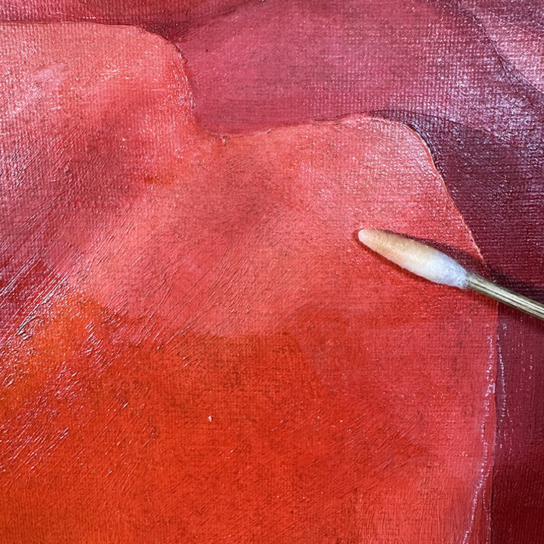 A close-up of a dirty cotton swab next to an oil painting.