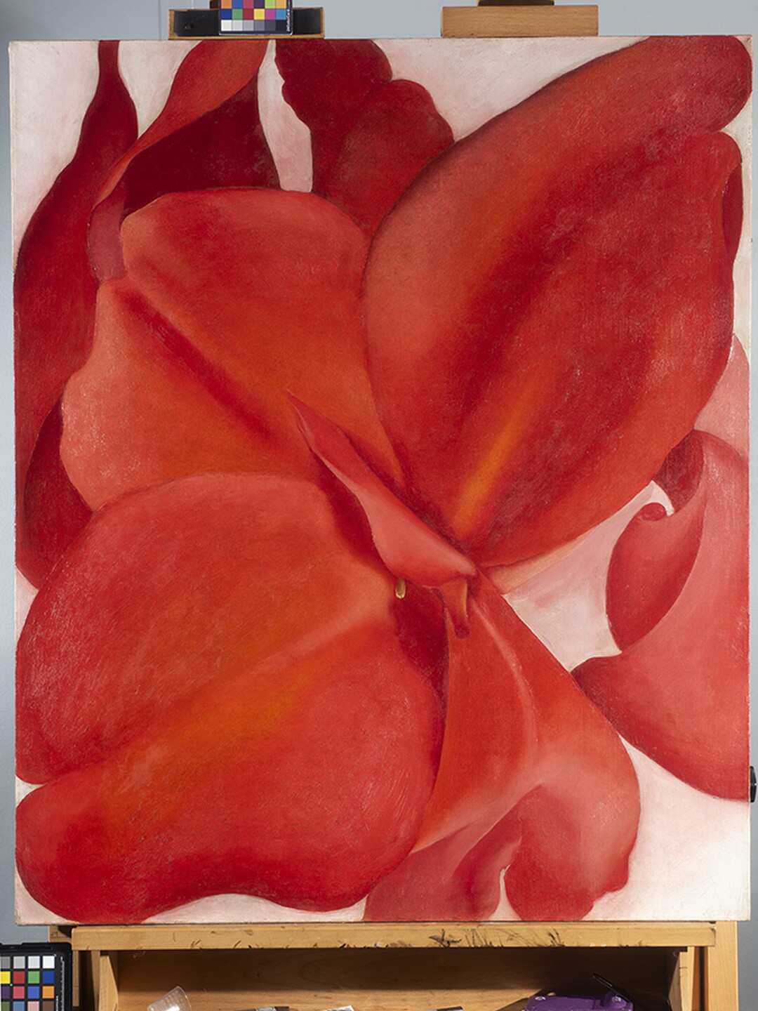 An oil painting on an easel of an extreme close-up, abstracted view of a red flower.