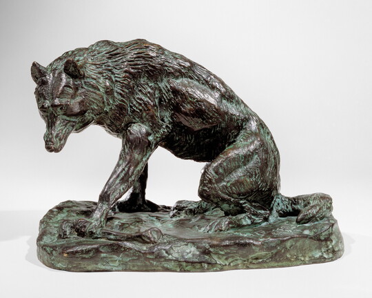 A bronze sculpture of a wolf crouching on its haunches.