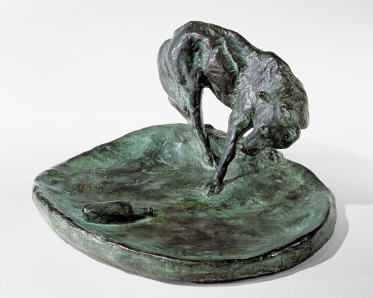 A bronze sculpture of a wolf staring at a bottle on the ground.