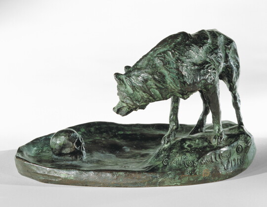 A sculpture of a wolf staring at a human skull on the ground.