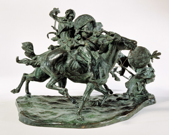 A bronze sculpture of two horses in mid-gallop, with both riders lunging toward a crouching man behind a shield.