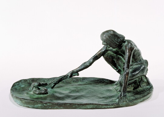A bronze sculpture of a squatting Indigenous man holding a stick in his outstretched arm toward a snake on the ground.