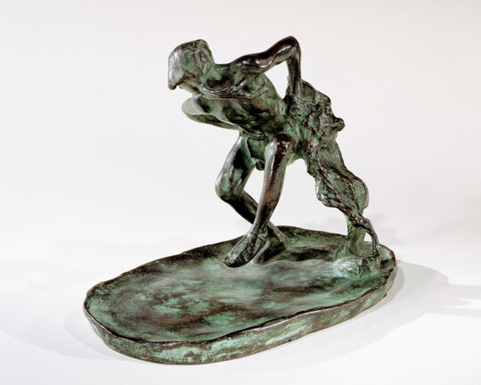 A bronze sculpture of an Indigenous man dancing with a wolfskin in his hand.
