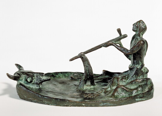 A bronze sculpture of a kneeling Native American man smoking a pipe in front of a bison skull.