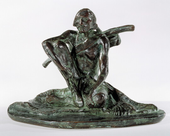 A bronze sculpture with a slight green patina of an Indigenous man seated on the ground.