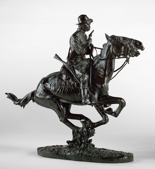 A bronze sculpture of a cowboy riding a galloping horse and holding a pistol close to his chest.