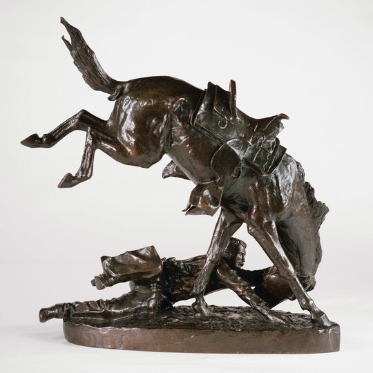 A bronze sculpture of a man on the ground hanging on to the head of his bucking horse.