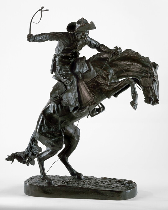 A bronze sculpture of a cowboy balancing on a rearing horse.