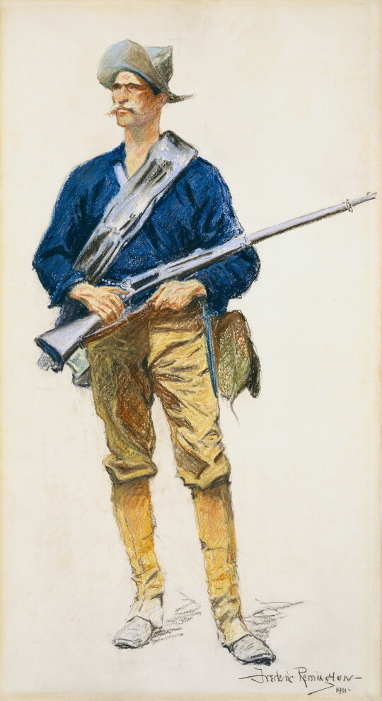 A color portrait of a standing White man wearing a hat, a blue blouse, khaki pants, and holding a rifle.