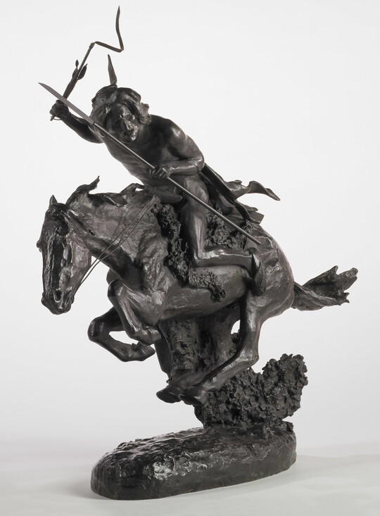 A bronze sculpture of an Indigenous person crouched on a running horse holding a spear and a whip.