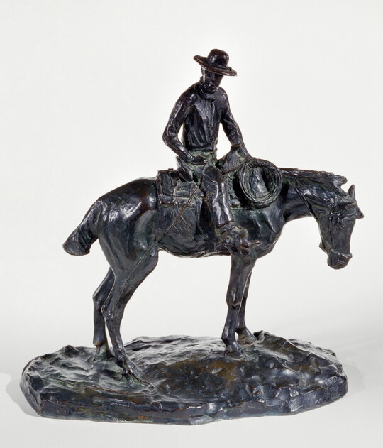A bronze sculpture of a man wearing a cowboy hat seated on a standing horse.