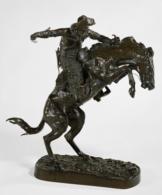 A bronze sculpture of a cowboy balancing on a rearing horse.
