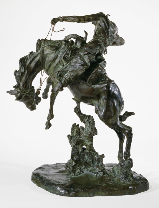 A bronze sculpture of a cowboy on horseback holding the reins as the horse raises up on its hind legs.