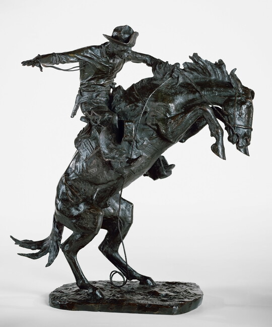 A bronze sculpture of a cowboy balancing on a rearing horse.