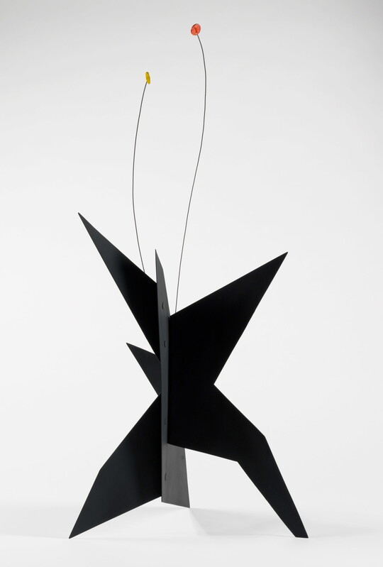 A black, metal, star-like shaped sculpture with two wires rising from the top, one capped with a yellow circle and the other with an orange circle.