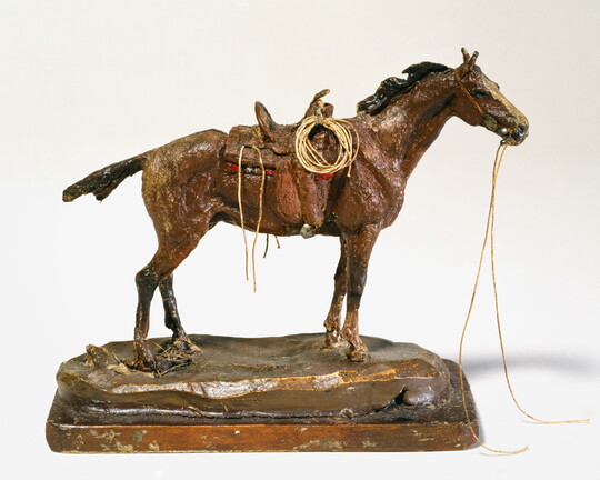 A sculpture of a standing, saddled horse with reins falling from the bridle.