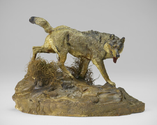 A painted sculpture of a wolf walking across patches of grass on a rock.