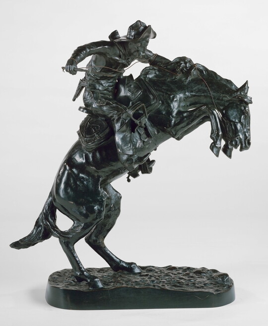 A bronze sculpture of a cowboy balancing on a rearing horse.