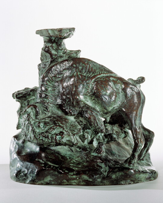 A bronze sculpture of a bison, head bent toward the ground, leaning against what might be a tree trunk to scratch its shoulder.