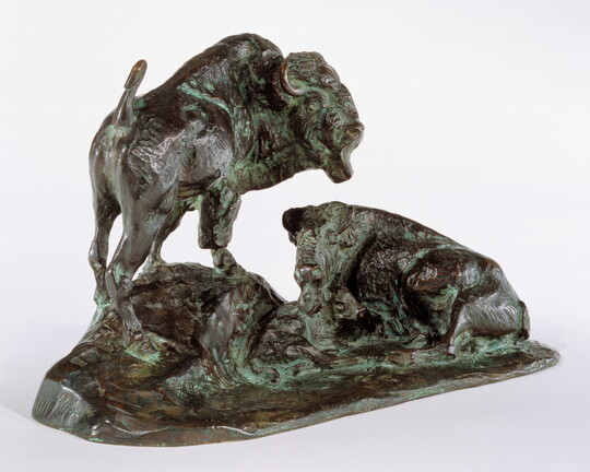 A bronze sculpture of two bison, one lying down and the other standing.