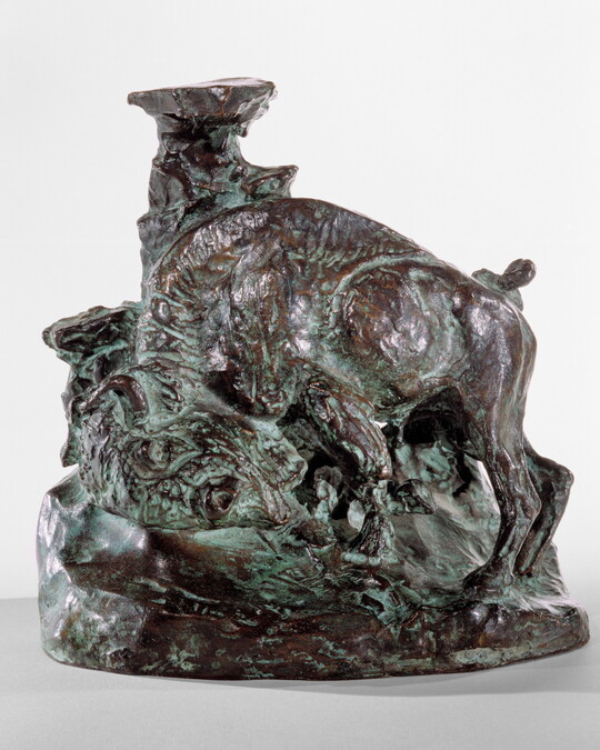 A bronze sculpture of a bison, head bent toward the ground, leaning against what might be a tree trunk to scratch its shoulder.
