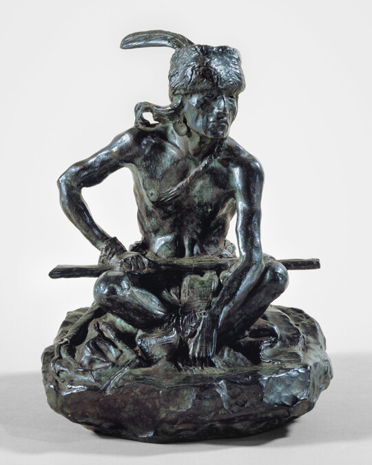 A bronze sculpture of an Indigenous man seated on the ground with a rifle resting across his lap.