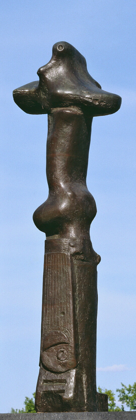 A tall, vertical, bronze sculpture of organic forms atop a geometrically carved base.