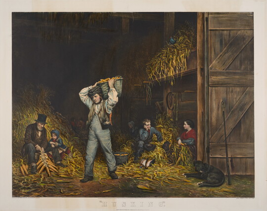 A color print of a group of White people of various ages husking corn in a barn; discarded husks piled in heaps around them.
