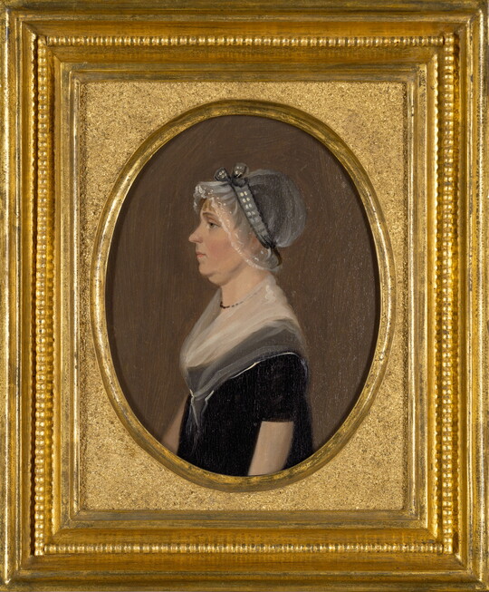 An oil painting in a gold frame of a White woman in profile wearing a sheer bonnet and black dress with a sheer scarf around her neck and shoulders.