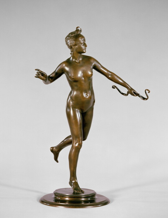A bronze sculpture of a nude, female archer in motion.