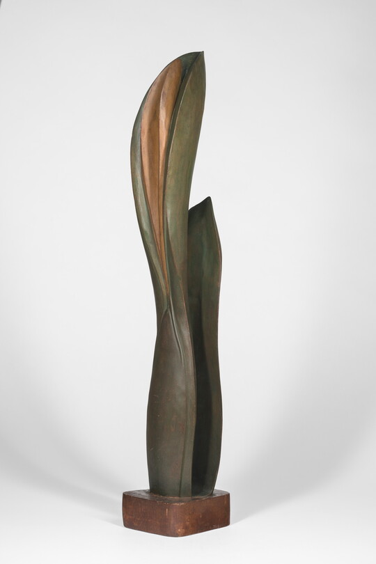 A wood sculpture of a tall, thin leaf with two smaller leaves on either side.