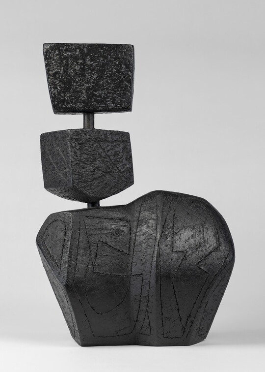 A black ceramic sculpture of three abstract, rectangular shapes, the largest on the bottom, connected vertically by a rod.