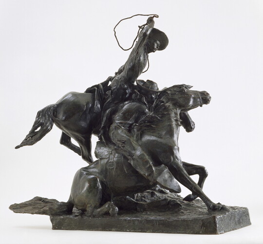 A bronze sculpture of a cowboy on horseback who is about to lasso another horse, its rider holding onto its neck, that is on the ground.