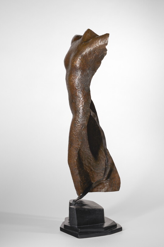 A copper sculpture of a nude female figure with no head, arms, or feet.