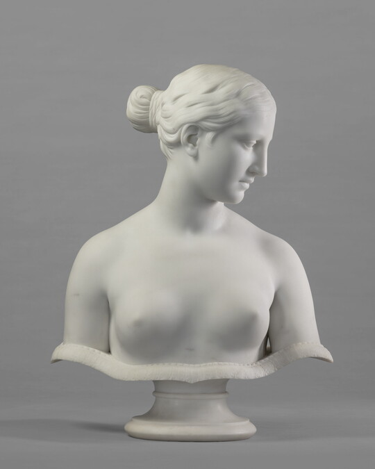 A marble bust of a bare-breasted woman, hair pulled up into a bun on the back of her head.
