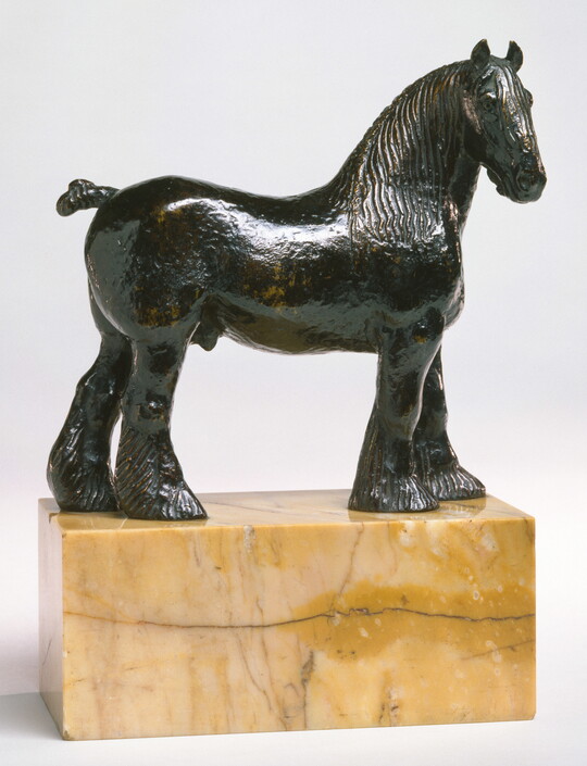 A bronze sculpture of a stallion with a bobbed tail and long hair on its legs below the knees standing on a stone base.
