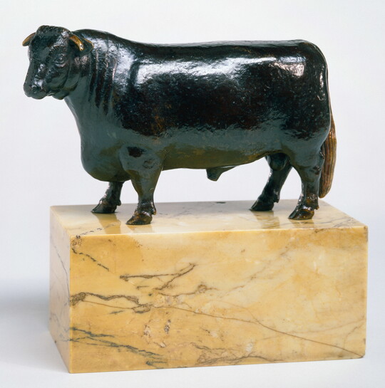 A bronze sculpture of a bull with a thick body and chest standing on a stone base.