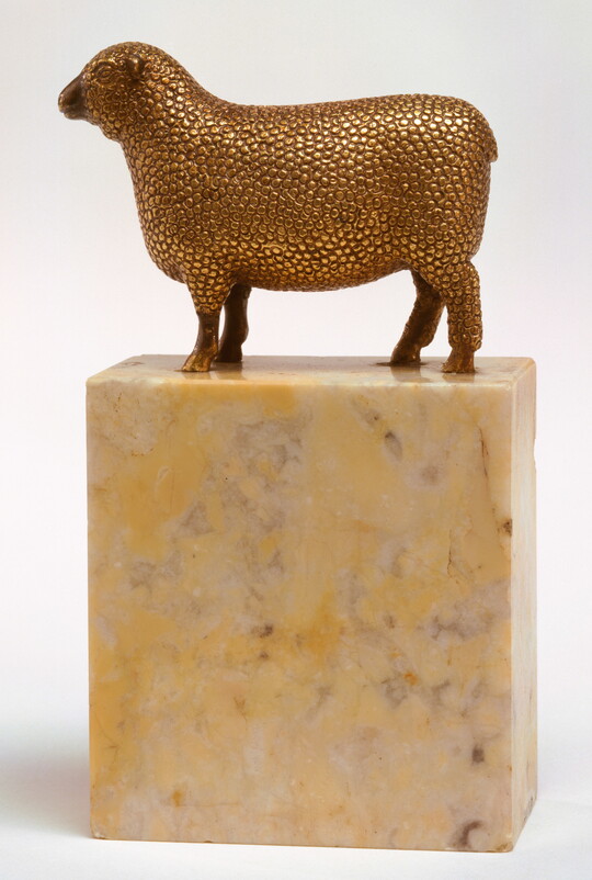 A bronze sculpture with a gold finish of a wooly sheep standing on a stone base.