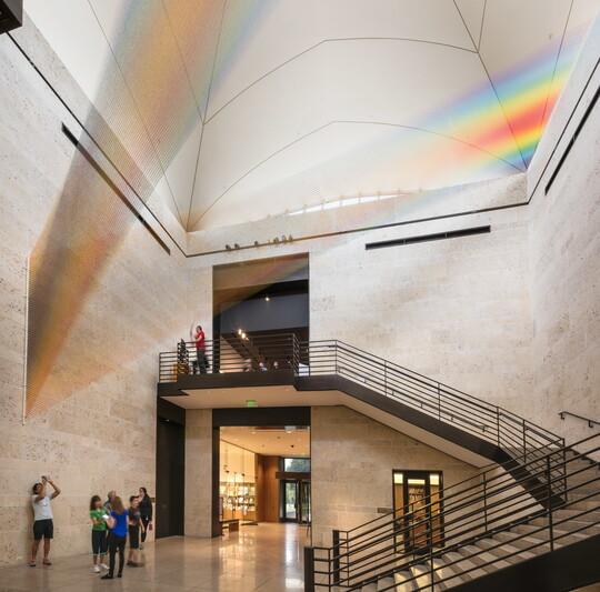 A large installation of multicolored sewing thread that stretches from one wall to the ceiling in the Carter's Atrium and looks like a rainbow.