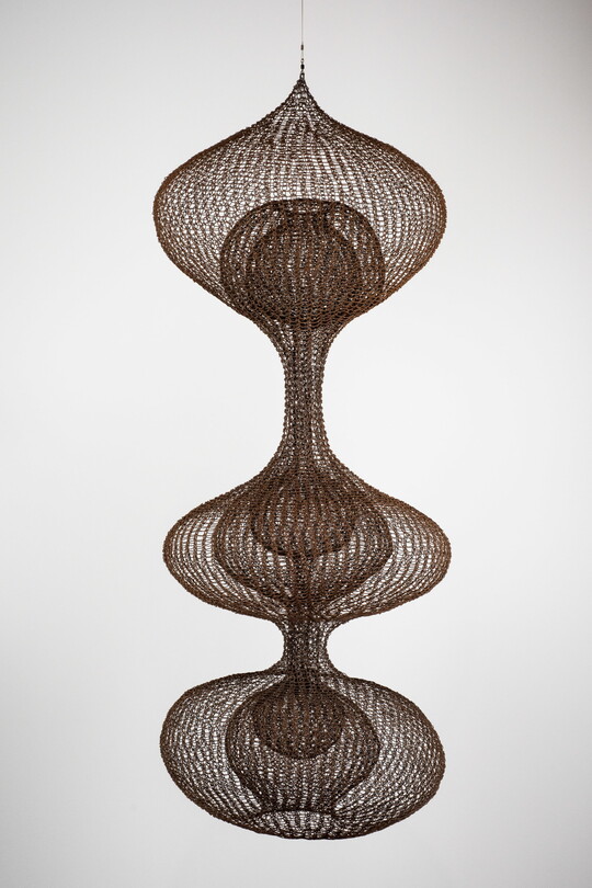 A hanging sculpture made of woven wire thread that creates three orb like shapes with smaller orbs nested inside each.