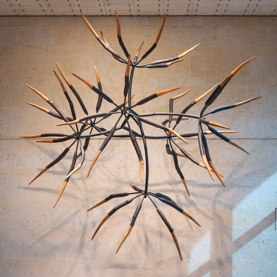 A large, hanging sculpture of seven clusters of seven elongated, tapered forms that resemble flower petals and stems.