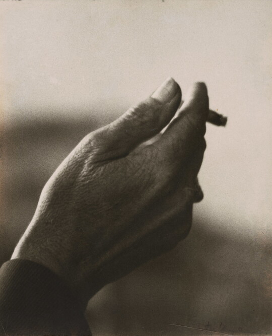 A sepia-toned close-up photograph of a right hand holding an almost-finished cigarette.